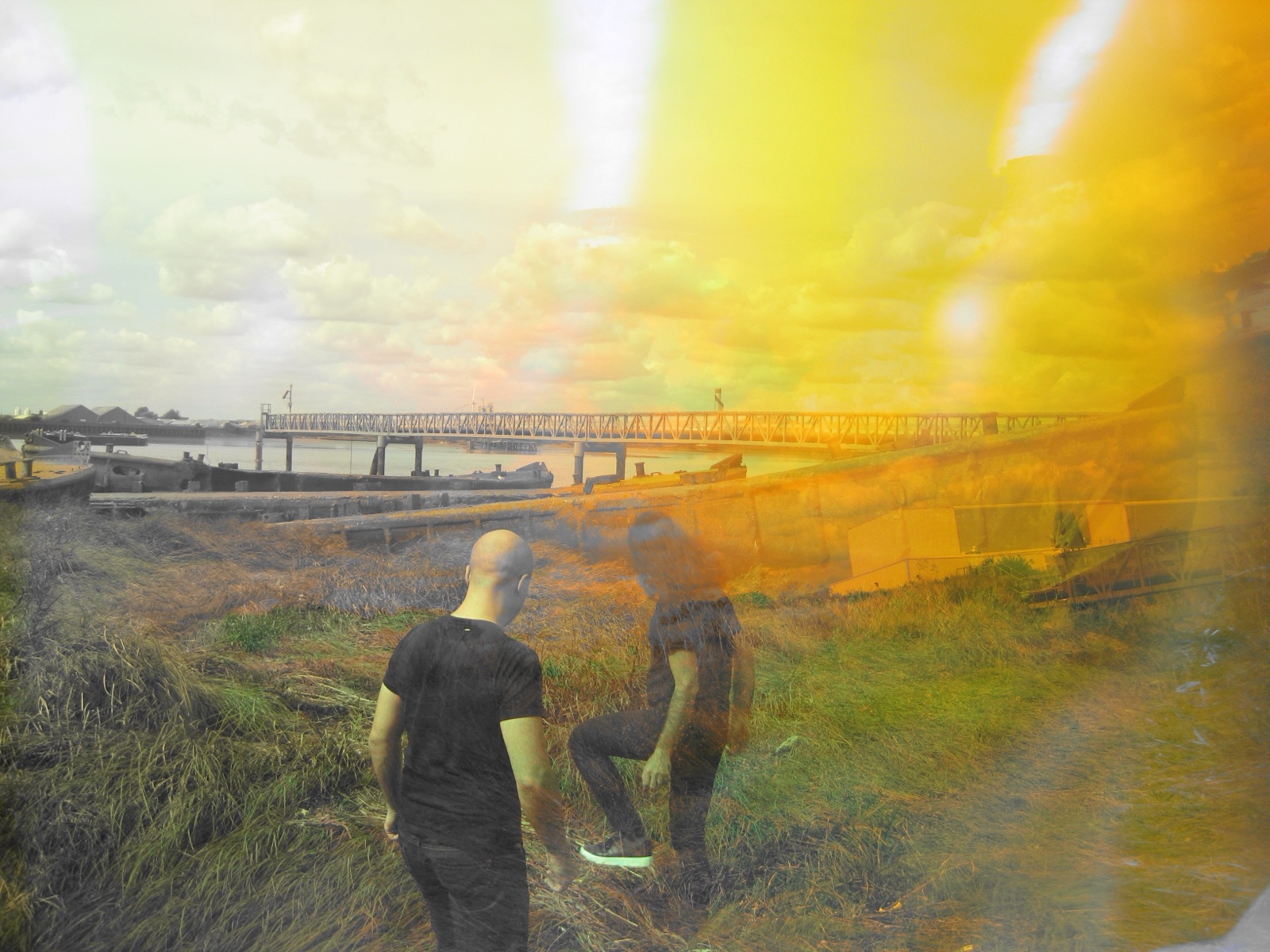 One musician is seen from behind while the other appears in overlapping translucent positions across a yellow waterfront landscape.