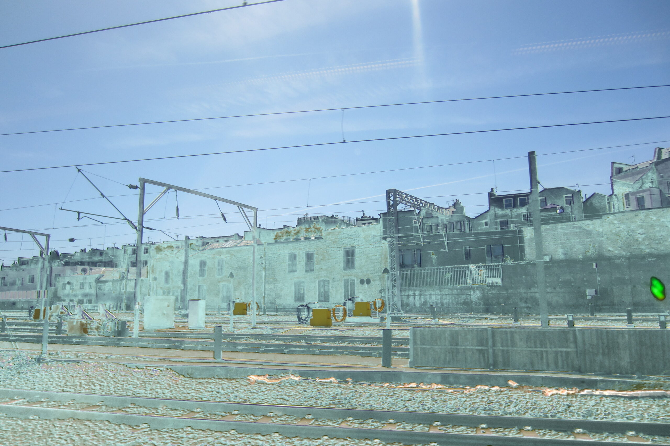 Railway landscape under blue sky with a faint carriage-light reflection.