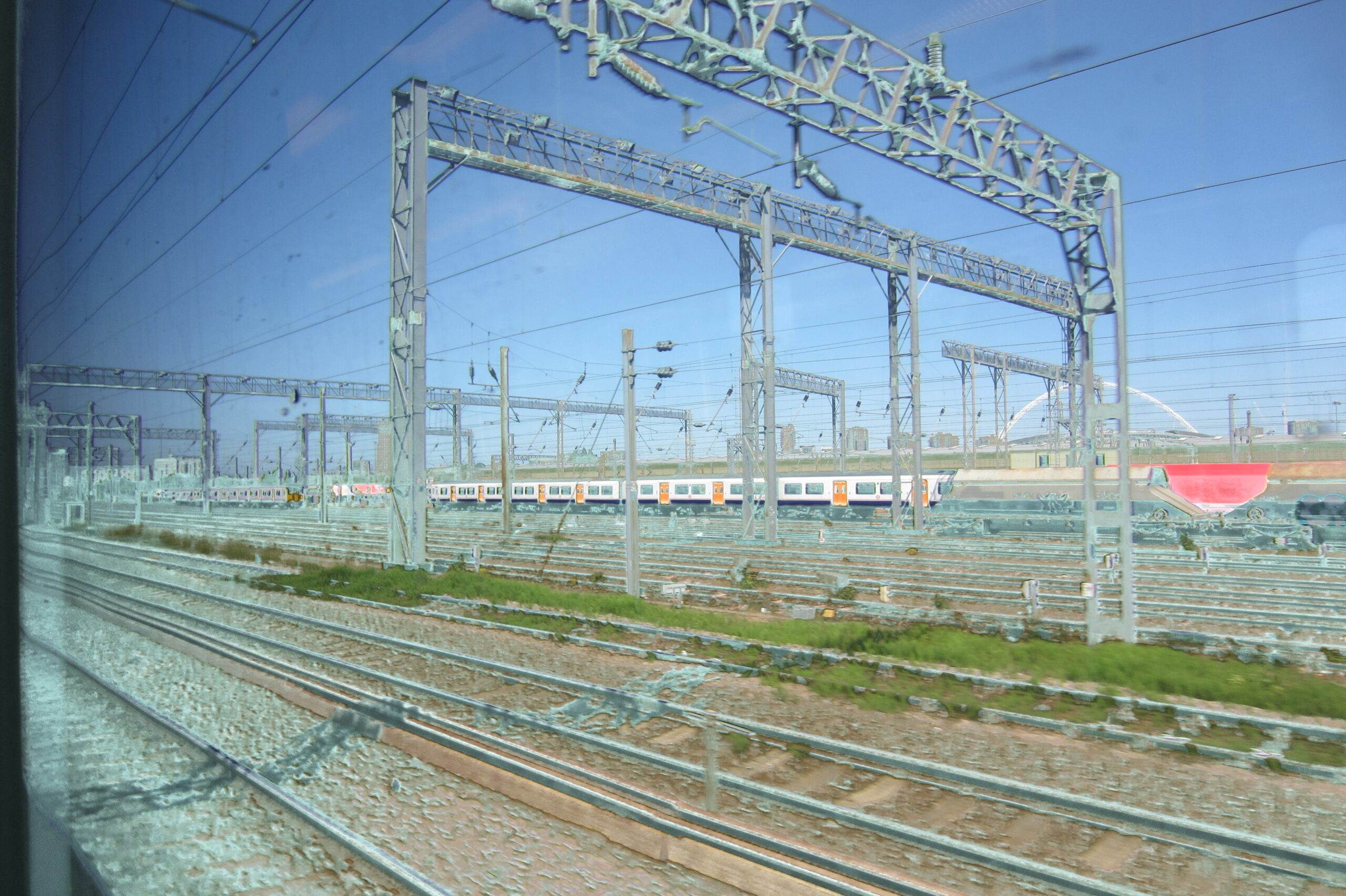 Rail yard filled with tracks, cables and trains beneath blue sky.
