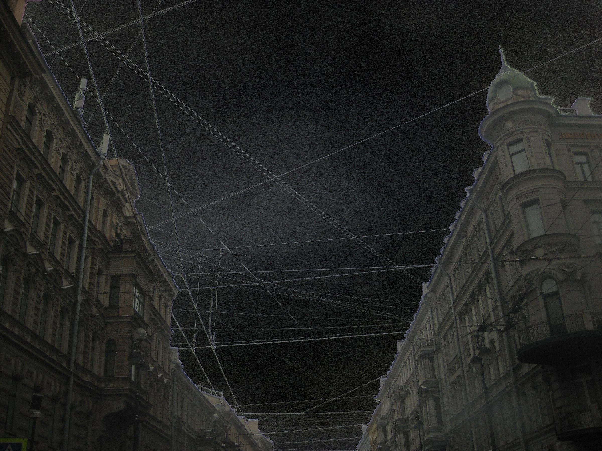 Overhead wires cross between city facades under a nearly black sky.