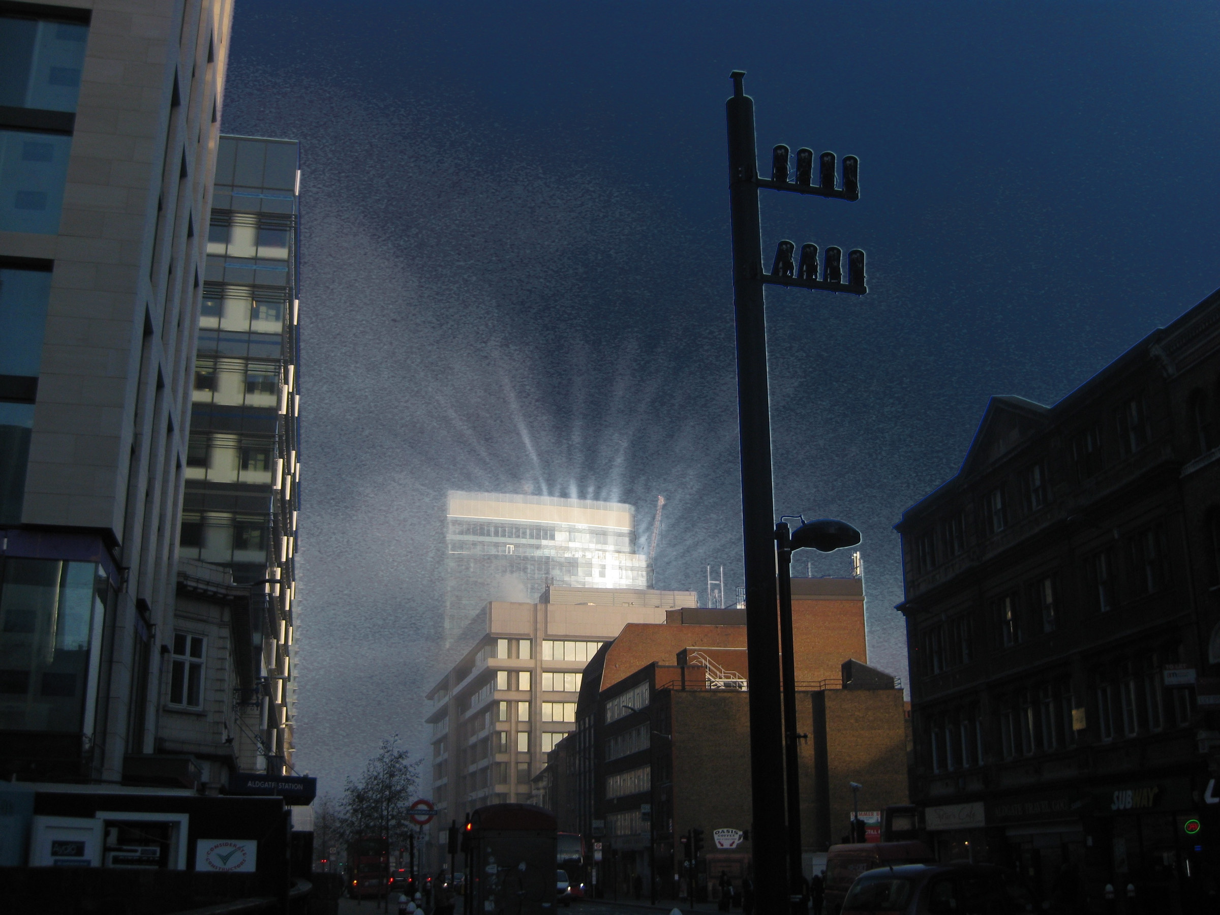 A bright flare rises between city buildings beneath a deep blue sky.