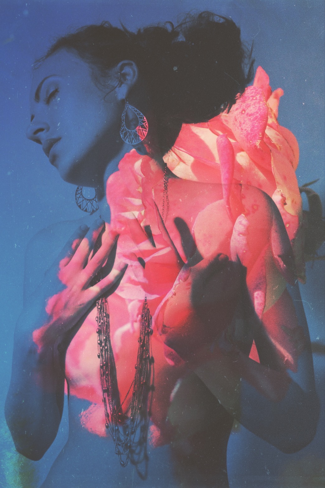 A portrait with raised hands and long necklaces, layered with a large pink rose across the neck and torso against a blue background.