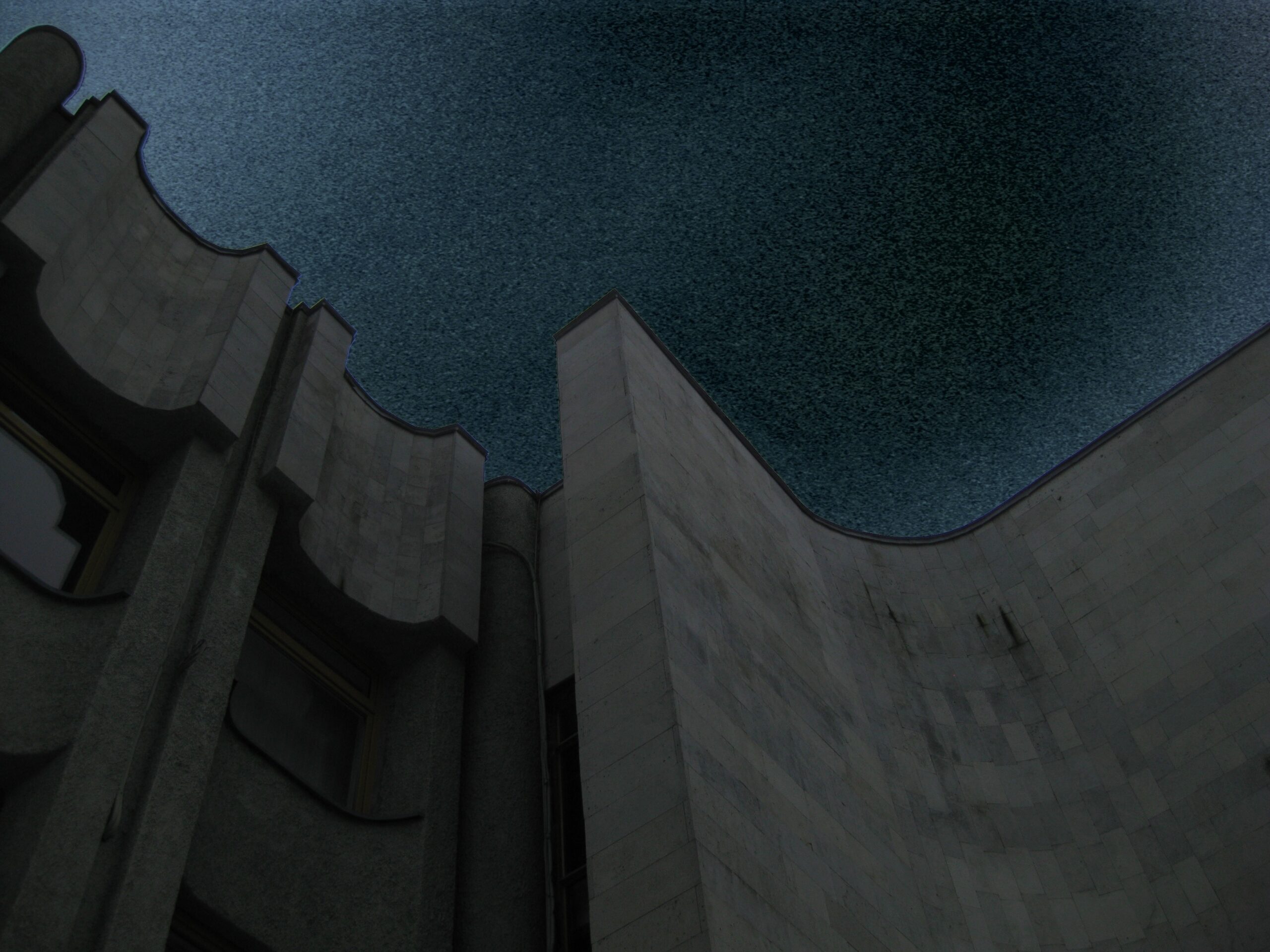 Pale curved concrete walls enclose an opening of blue-black grainy sky.