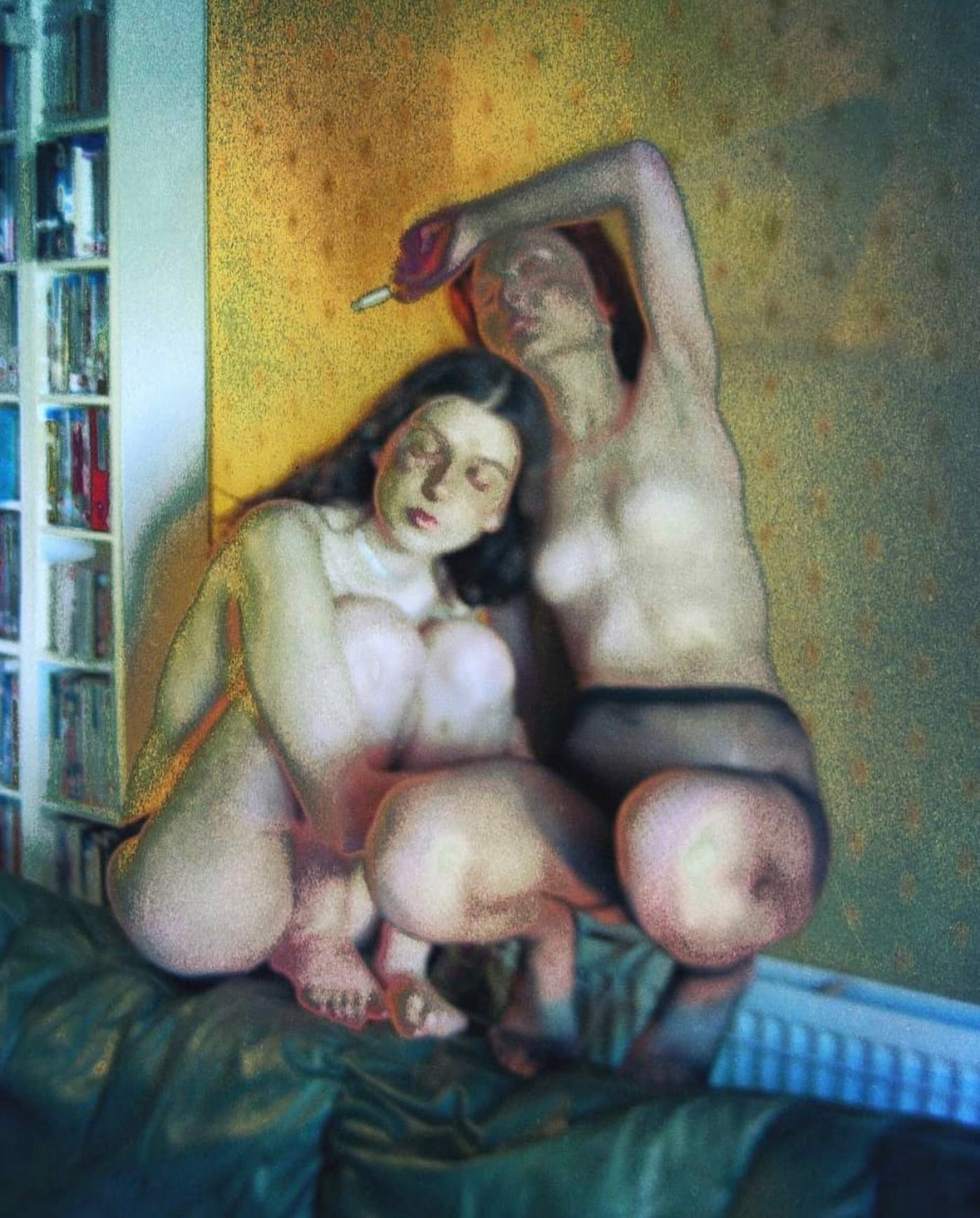 Two women sitting closely together on a green sofa beside shelves of books and CDs.